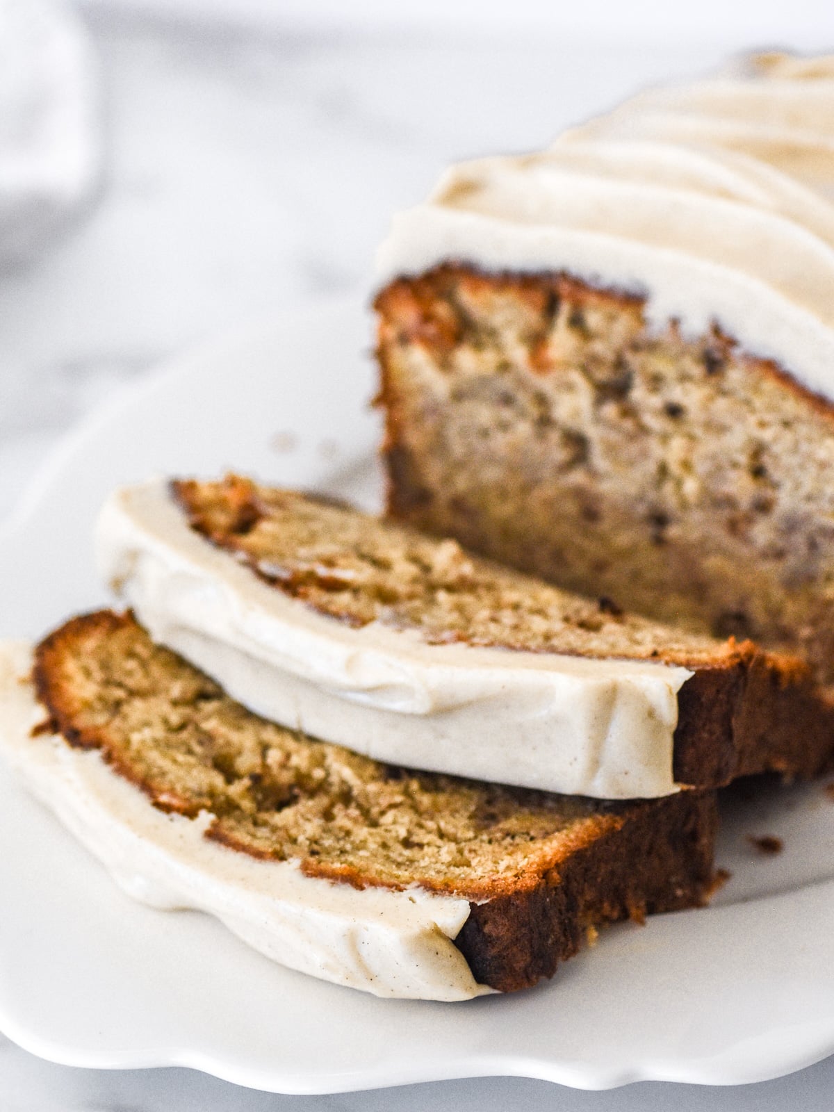 Cinnamon Cream Cheese Frosting shown on a banana bread loaf. Photo taken from the side with slices of banana bread falling.