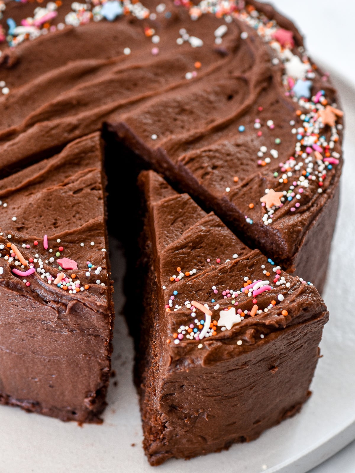 Whole mini chocolate cake with chocolate frosting shown from above. One slice has been cut.