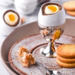 Cheesecake filled chocolate easter egg on a plate next to sugar cookies,