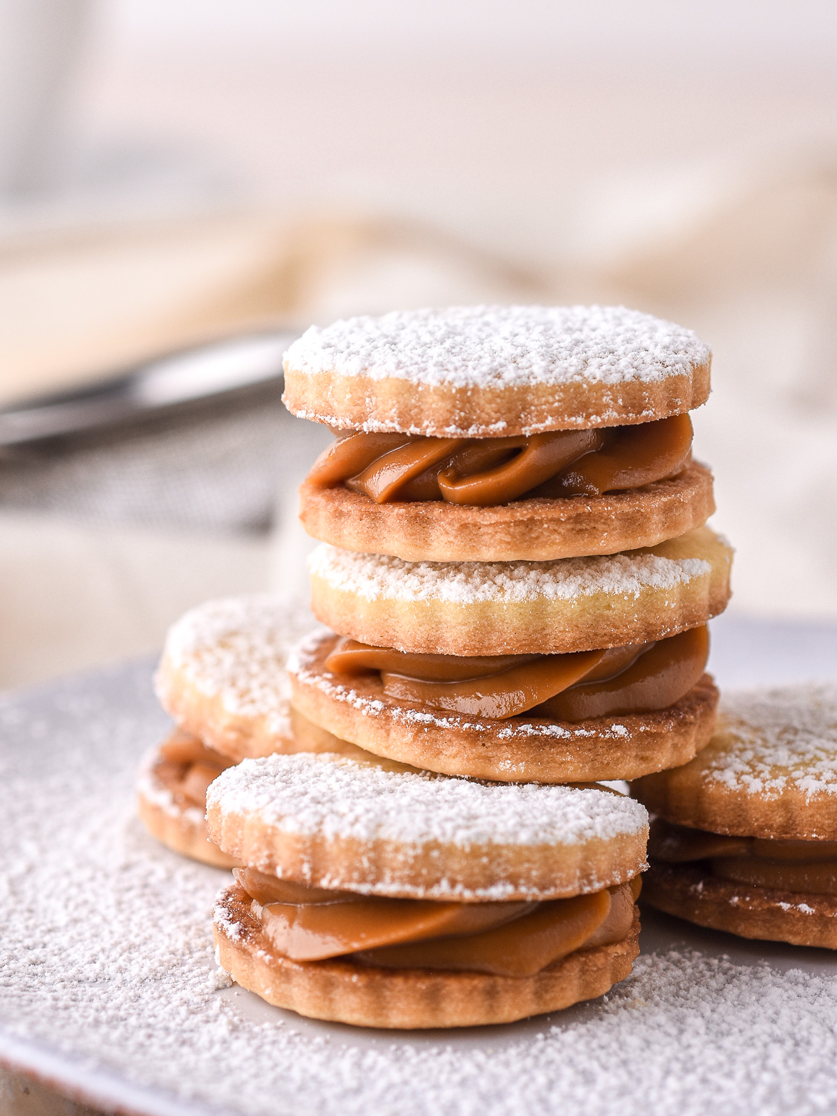 Caramel-filled sandwich cookies dusted with icing sugar shown on a plate. 