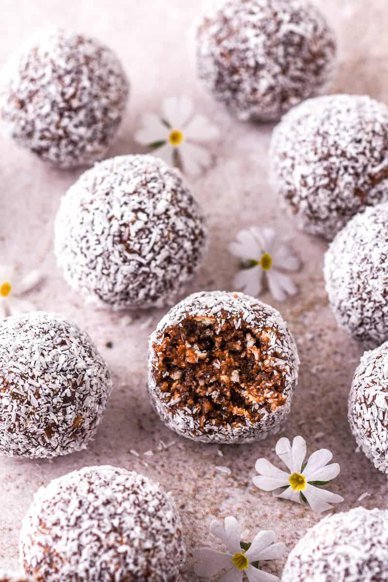 Condensed Milk Chocolate Truffles shown on a kitchen counter with desiccated coconut and small white flowers. One of the truffles have been bitten into.