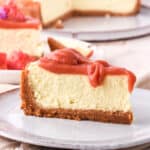 Guava cheesecake slice shown on a plate with the full cheesecake in the background of the photo.