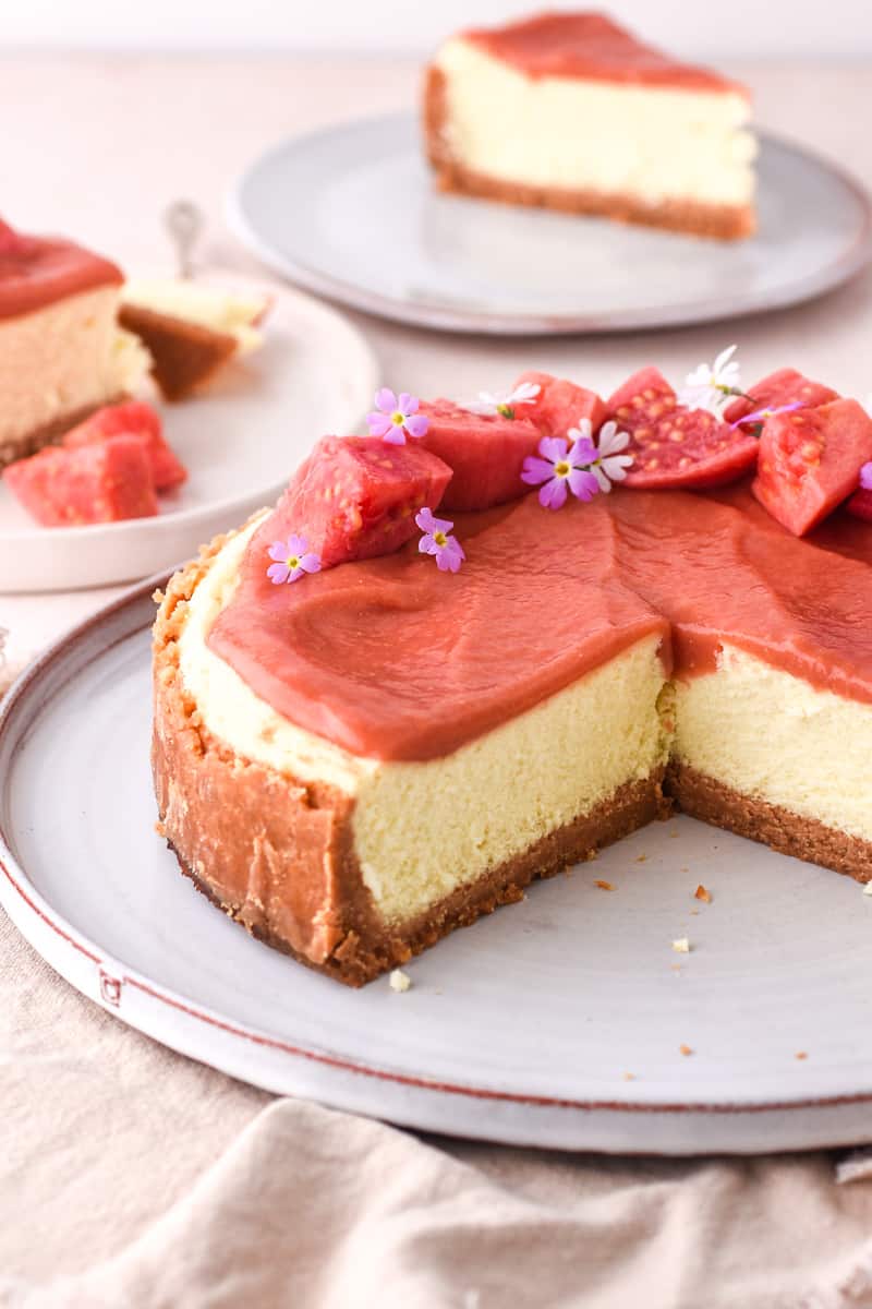 Guava Cheesecake shown on a cake plate with about a quarter of the cheesecake already sliced. 
