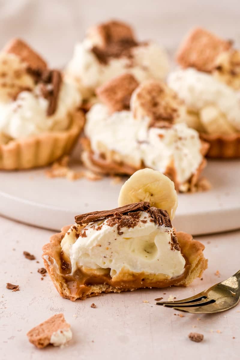 Banoffee Tartlets shown on a kitchen counter, one tart is cut in half so that you can see the layered ingredeints.
