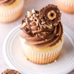 Vanilla Nutella Cupcake shown on a small white plate, it is decorated with chopped nuts and half a Ferrero Rocher Chocolate.