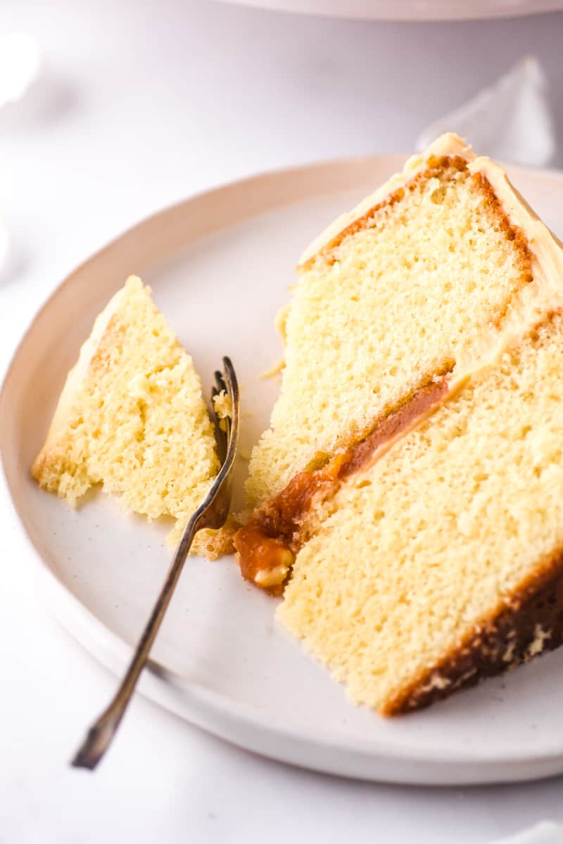 Salted Caramel Cake slice shown on a white plate with a fork through the slice of cake.