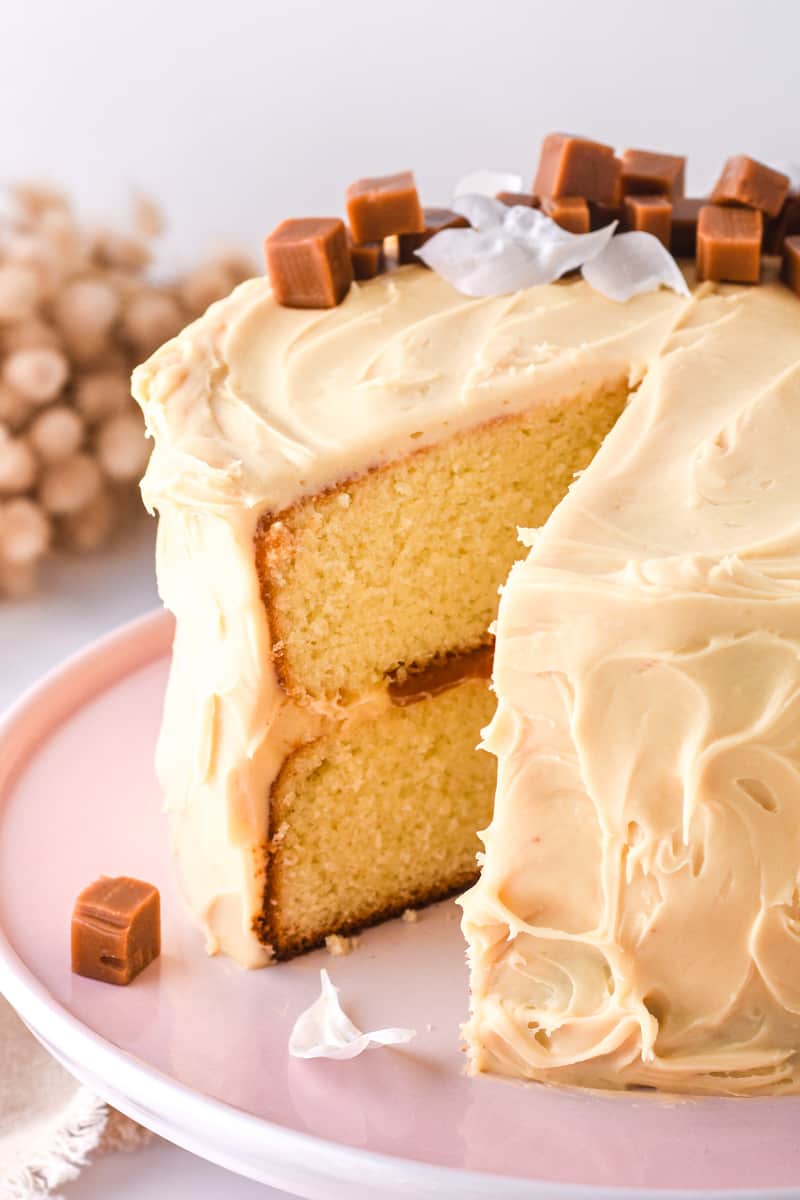 Salted Caramel Cake shown on a pink cake stand with caramel pieces on top of the cake.