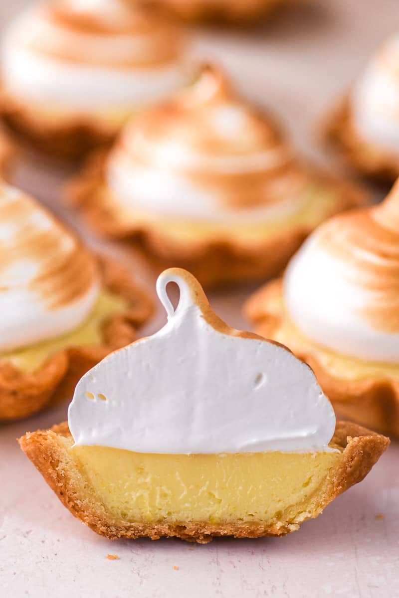 Mini Lemon Meringue Tart shown cut in half up close so that you can see the layer of pastry, lemon curd, and meringue topping 