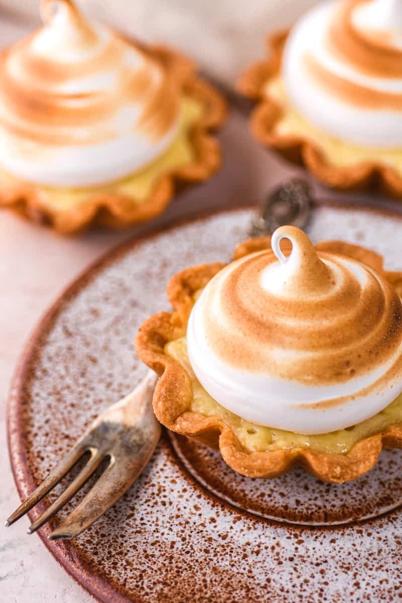 Mini Lemon Meringue Tart shown on a speckled plate next to a fork