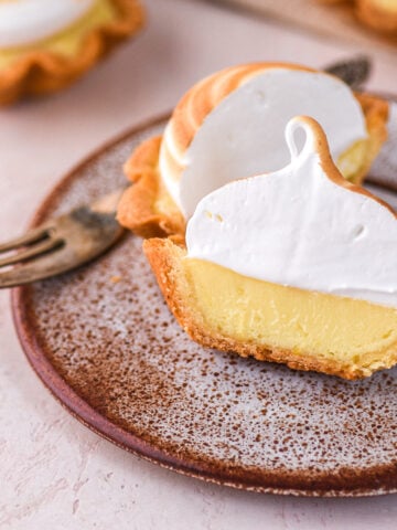 Mini lemon meringue tart shown sliced in half so that you can see the layer of pastry, lemon filling, and meringue.
