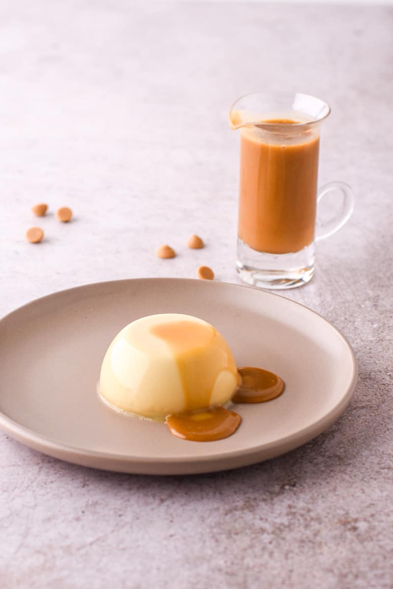 Baileys Panna Cotta shown on a light beige plate with chocolate sauce dripping off the dessert.