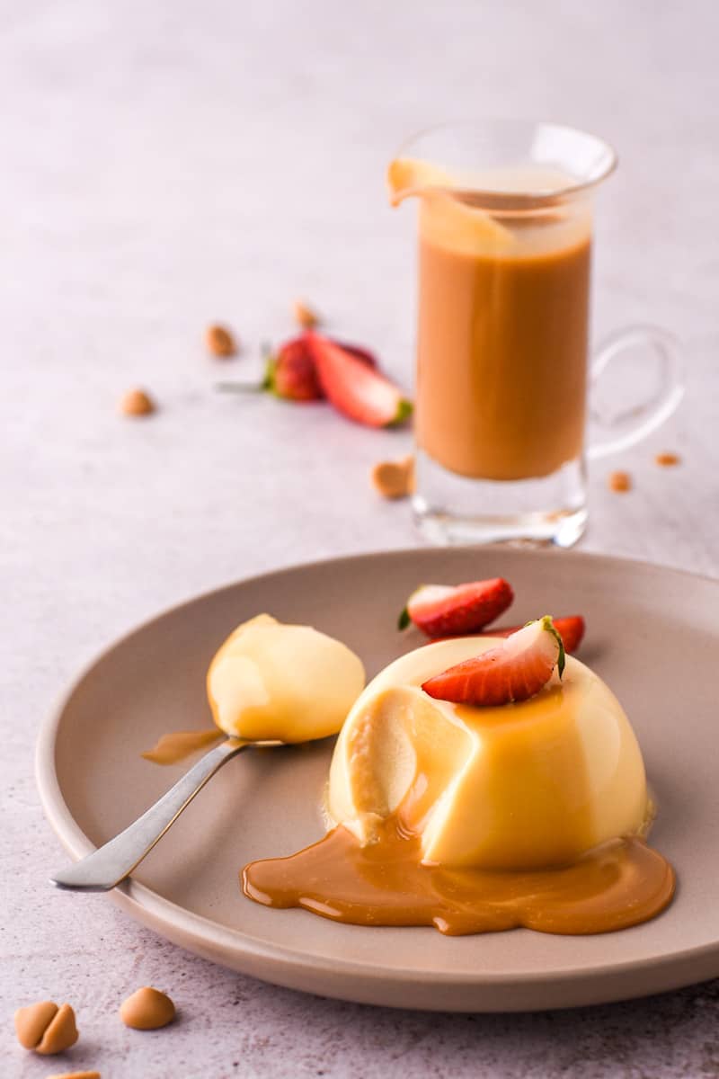 Baileys Panna Cotta shown on a plate next to a glass jar filled with caramel chocolate sauce.