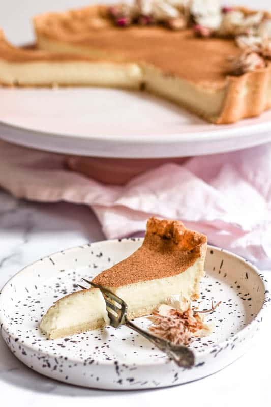 A slice of milktart shown on a plate with a fork through it.