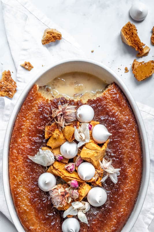 Malva pudding shown from above in an oval dish, with honeycomb and meringues on top of it.