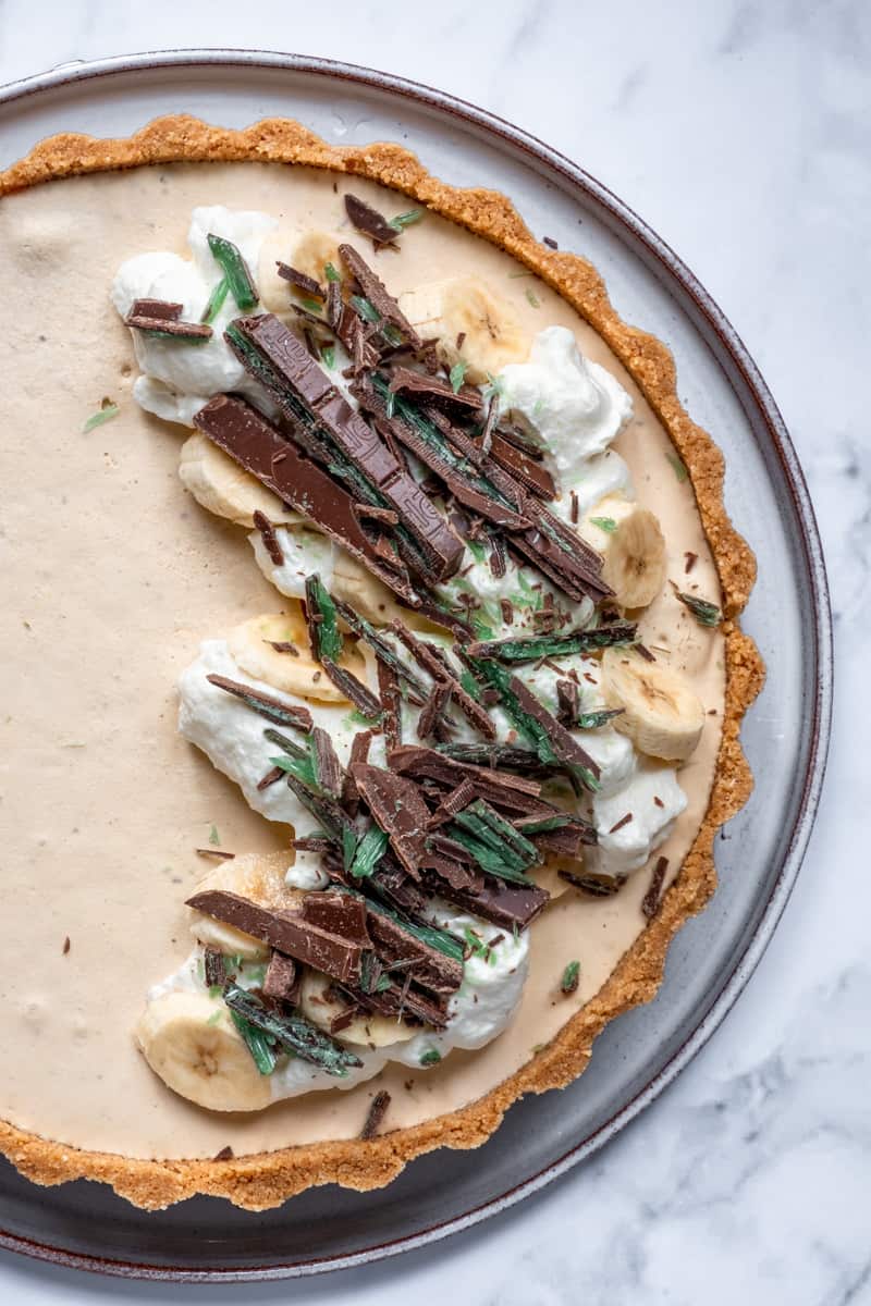 Peppermint crisp tart shown from above, the tart is topped with crushed chocolate, fresh cream, and bananas.