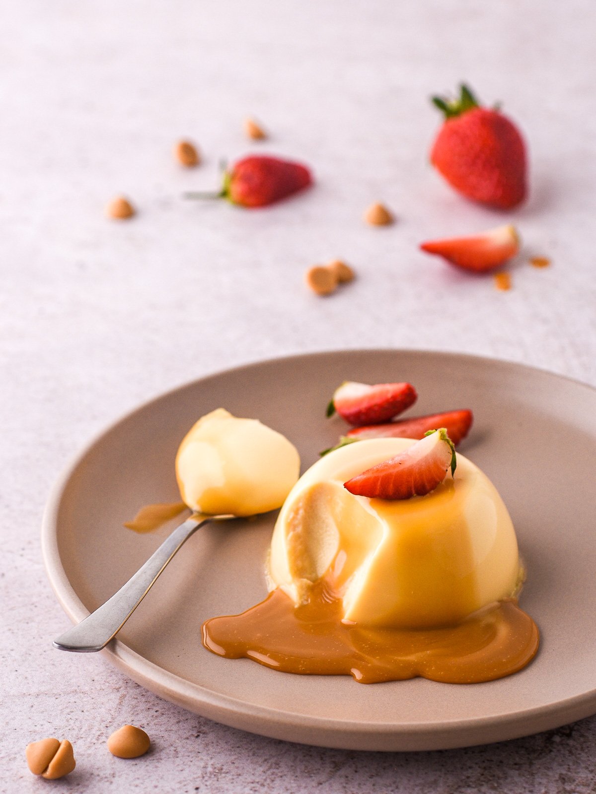 Baileys Panna Cotta shown on a plate with sliced strawberries on top of the dessert and in the background.
