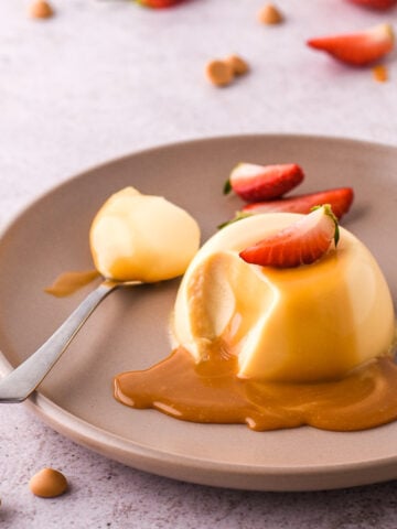 Baileys Panna Cotta shown on a plate drizzled with caramel chocolate sauce. There is a spoonful missing.