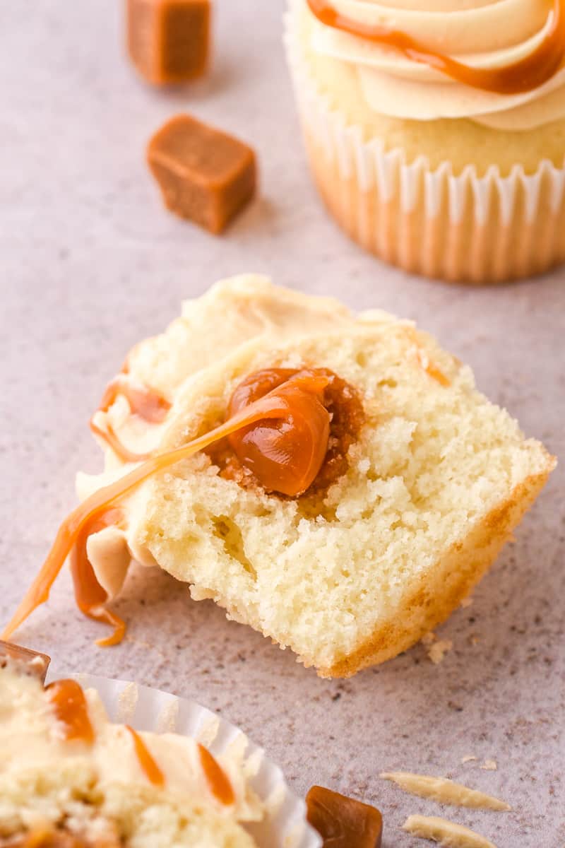 Photo showing a vanilla cupcake cut in half, you can see the Salted Caramel Buttercream and caramel filling of the cupcake.
