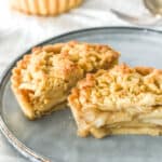 Mini apple crumble tarts shown on a kitchen counter. The one tart is cut in half and seen on a dusty blue plate.