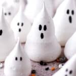 Mini ghost meringues shown on a kitchen counter with sprinkles.