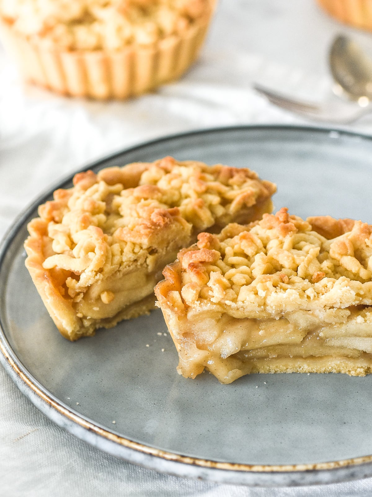 A Mini Apple Crumble Tart shown cut in half on a plate so that you can see the spiced apple filling inside.