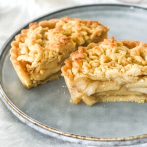 Image shows a mini apple crumble tart cut in half on a plate. You can see the spiced apple filling inside.