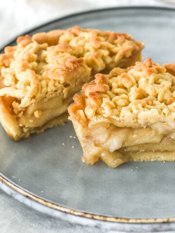 Image shows a mini apple crumble tart cut in half on a plate. You can see the spiced apple filling inside.