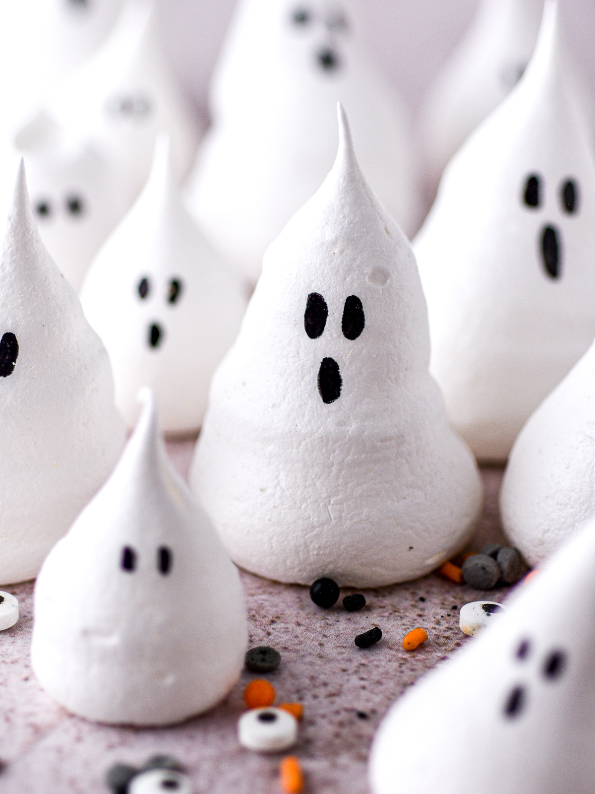 Halloween mini ghost meringues decorated with spooky eyes shown on a kitchen counter.