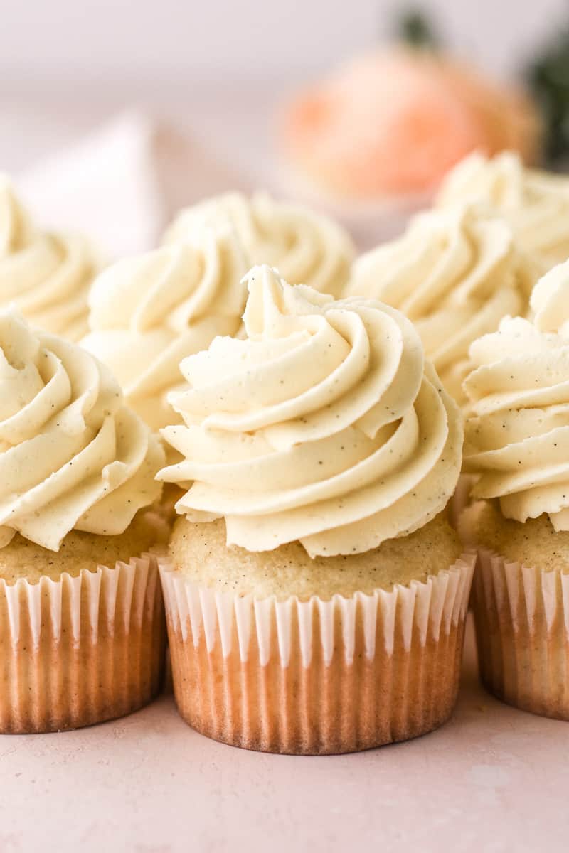 Vanilla Bean Cupcakes shown on a kitchen counter. You can see the vanilla bean frosting piped high on top of the cupcakes.