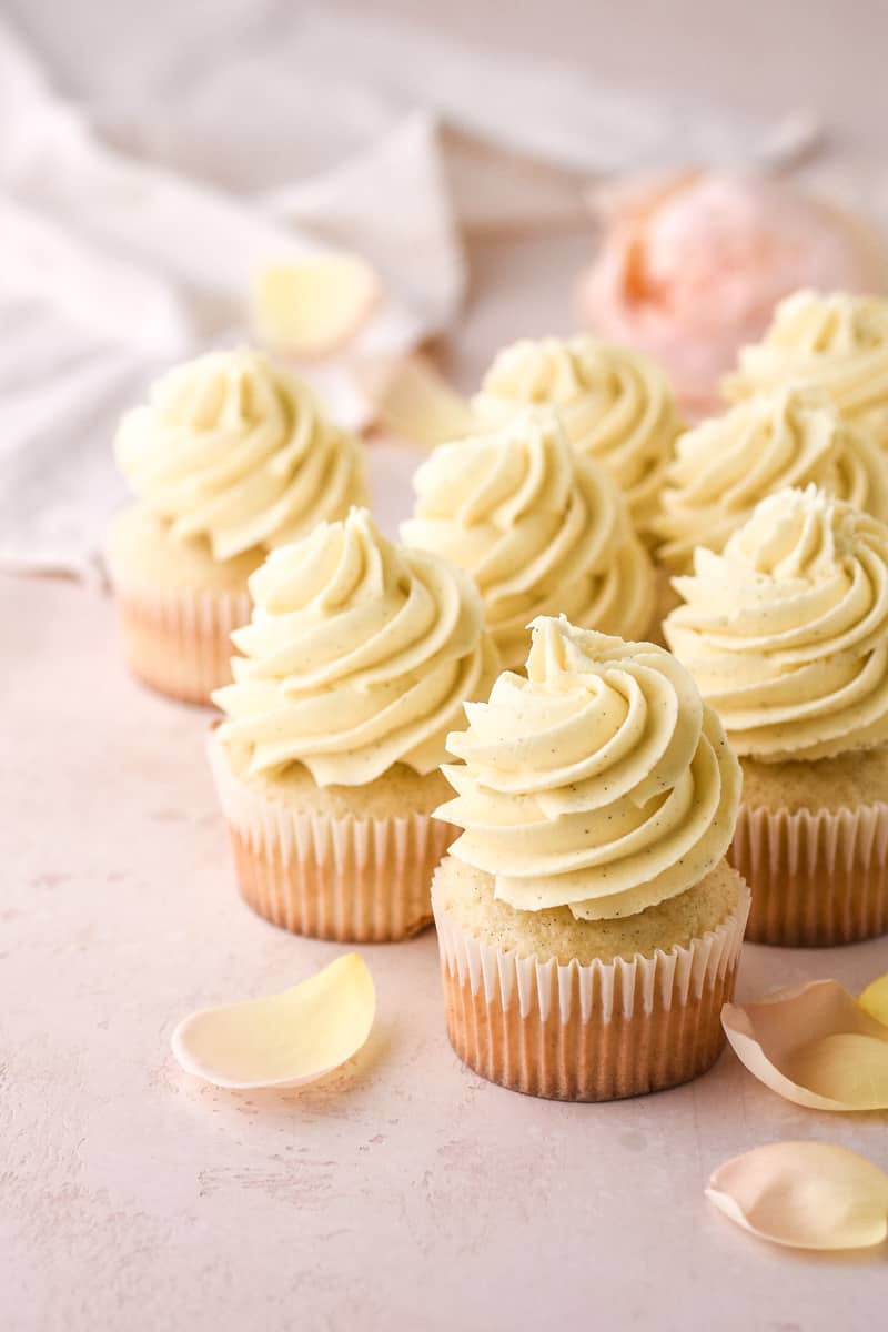 Vanilla Bean Cupcakes shown on a pink kitchen counter, then rose petals.
