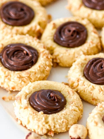 Nutella Thumbprint Cookies covered in crushed hazelnuts shown on a white plate.