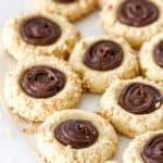 Nutella Thumbprint Cookies shown on a white plate with chopped hazelnuts.