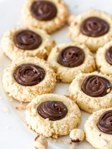 Nutella Thumbprint Cookies shown on a white plate with chopped hazelnuts.
