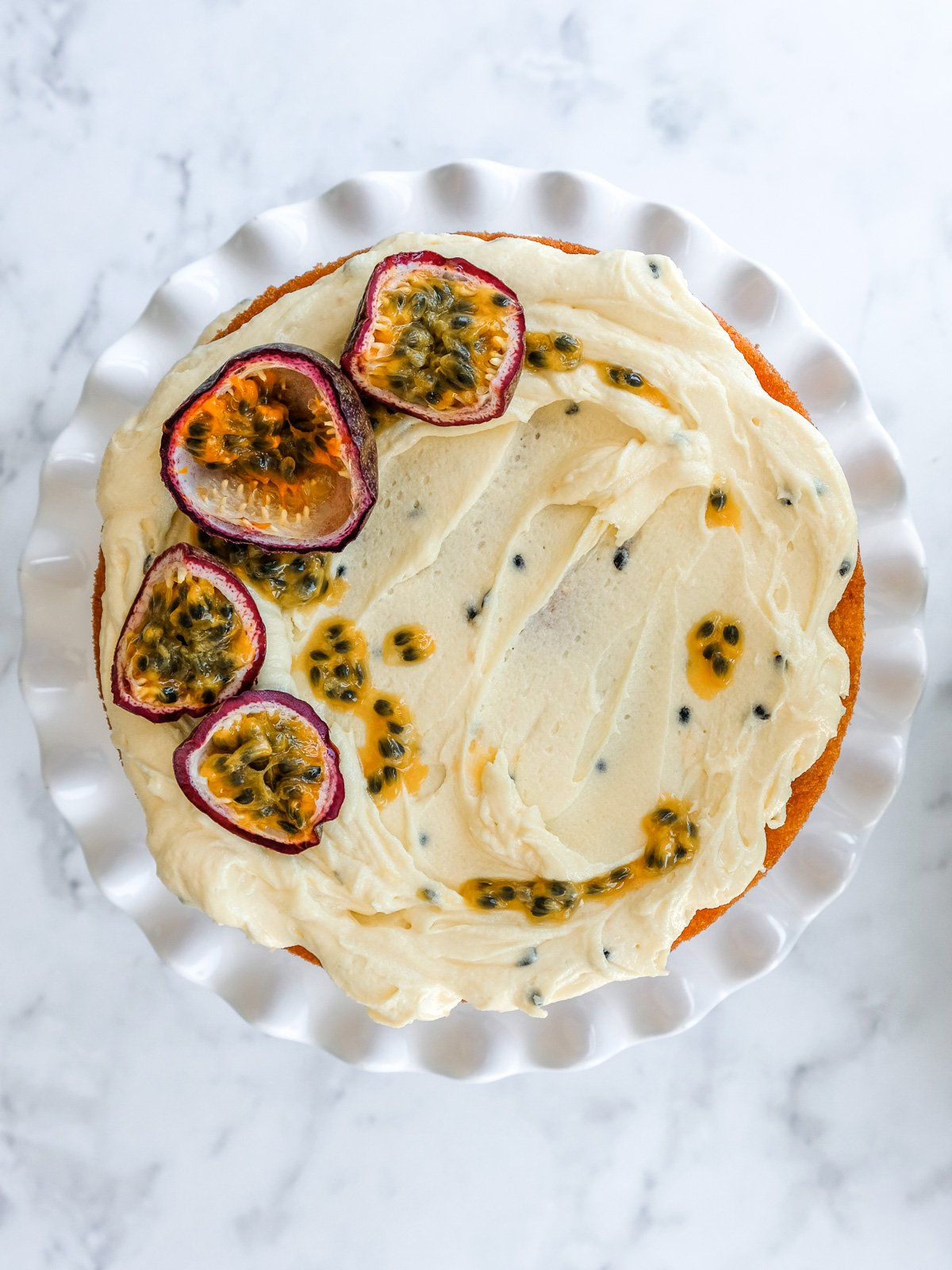 Image shows a cake from above that has been decorated with this passion fruit buttercream and fresh sliced passion fruits.