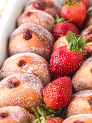 Strawberry donuts shown in a white serving dish with fresh strawberries.