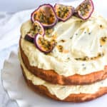 Passion Fruit cake shown on a white cake stand on a counter top. There are fresh passionfruit slices on top of the cake.