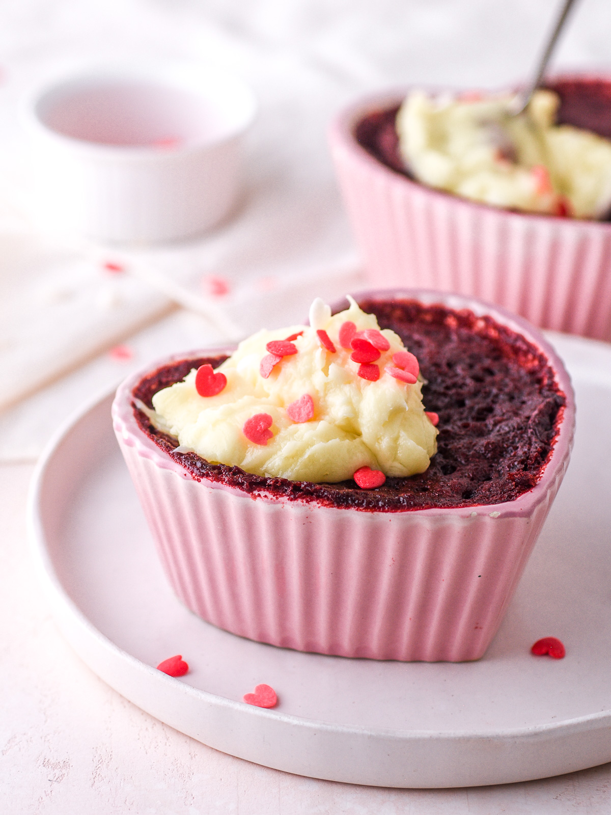 Red Velvet Mug Cake shown in a pink heart shaped ramekin set onto a white plate.