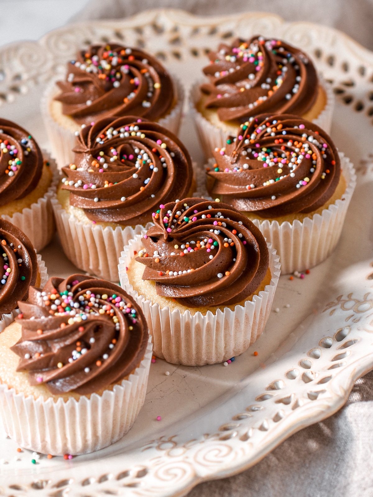 A white platter filled with vanilla cupcakes with chocolate frosting. You can see their perfect swirls of frosting.