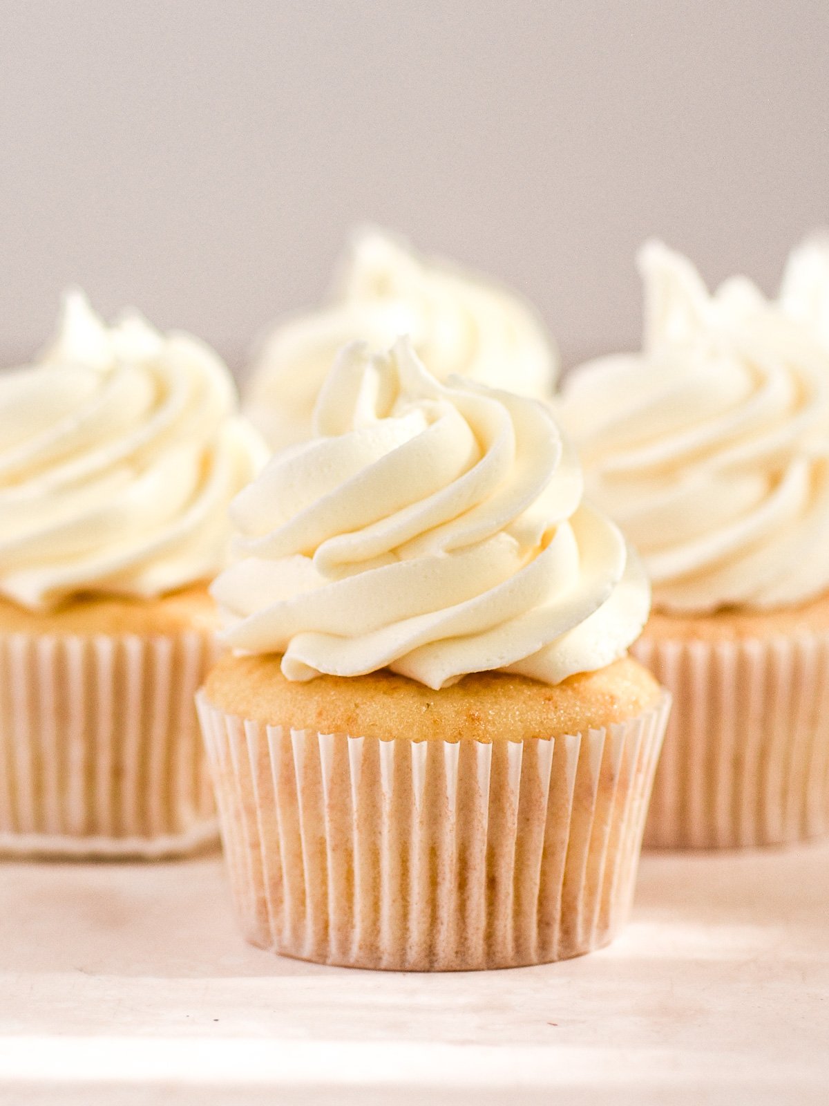 Vanilla cupcakes with oil shown on a countertop, you can see their perfectly dome tops and a big swirl of vanilla frosting.