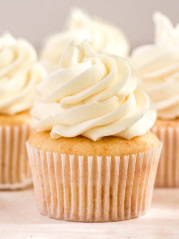 Image shows the vanilla cupcakes made with oil decorated with a large swirl of vanilla buttercream.