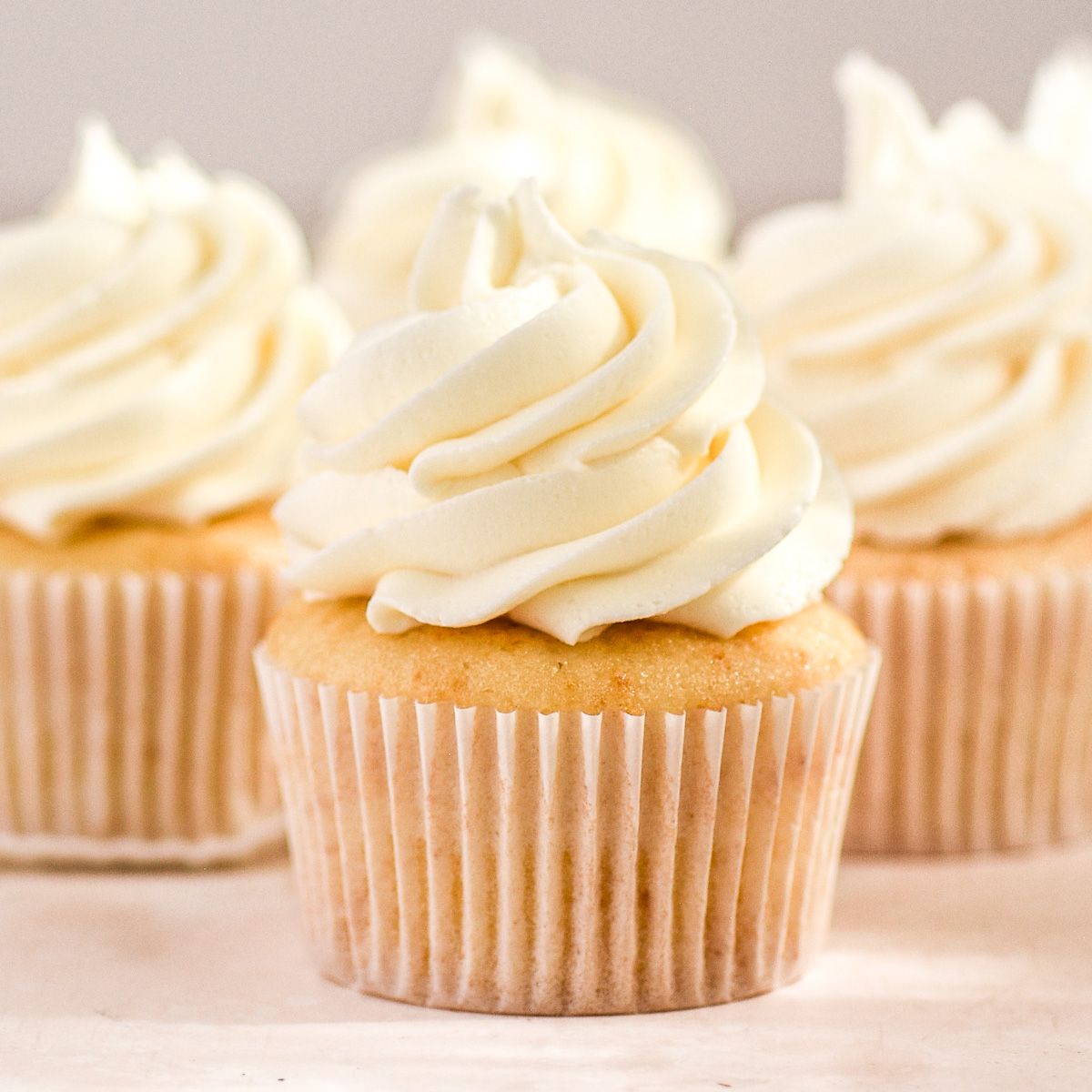 Image shows the vanilla cupcakes made with oil decorated with a large swirl of vanilla buttercream.