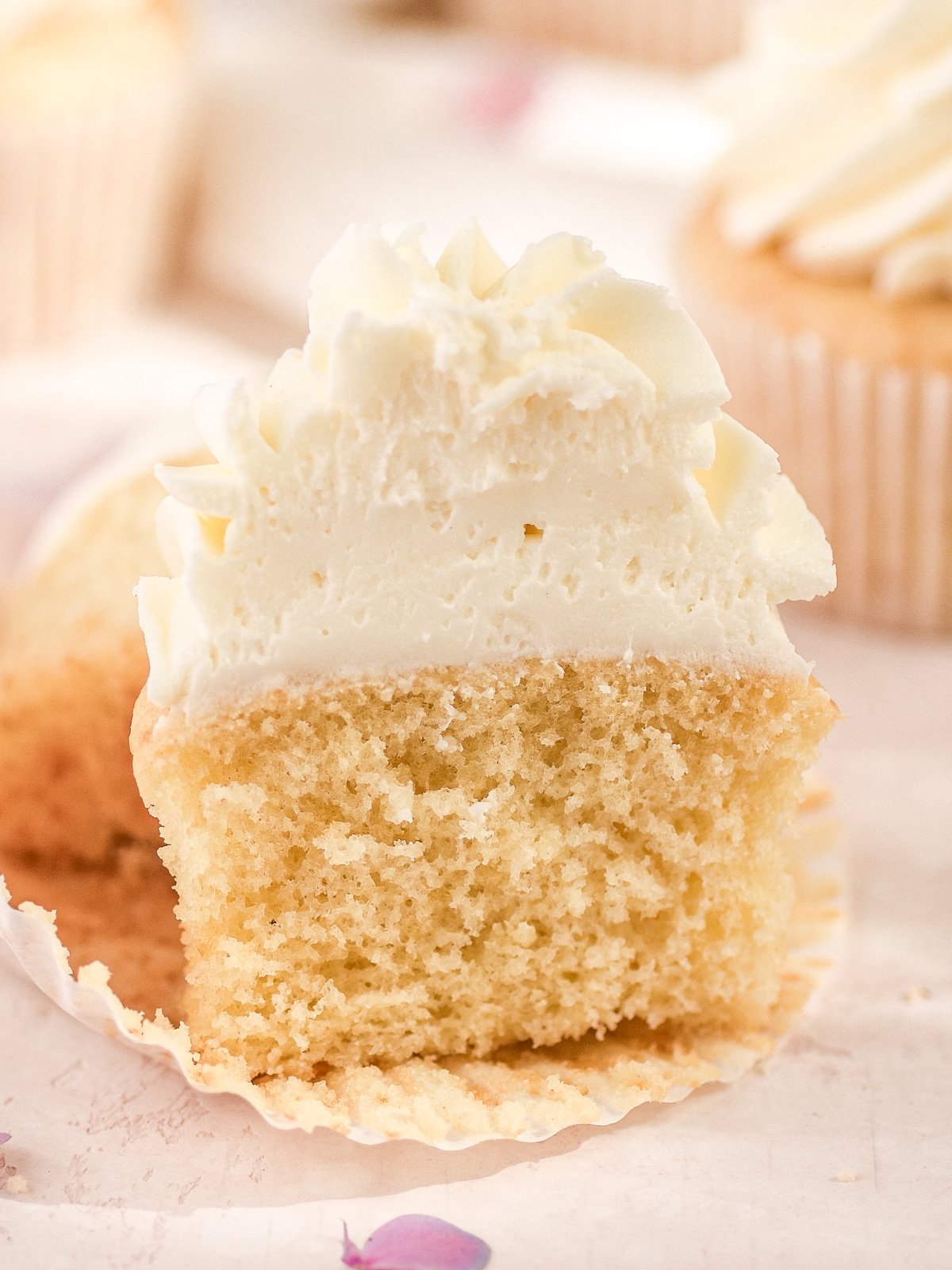 Image shows a vanilla cupcake sliced in half so that you can see the fluffy texture of the cupcake inside.
