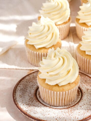 Vanilla Cupcakes with Oil shown on a pink counter top, the cupcake in the front is on a speckled plate.