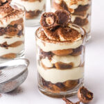 Mini tiramisu cups shown on a white counter they are decorated with Ferrero Rocher chocolates.