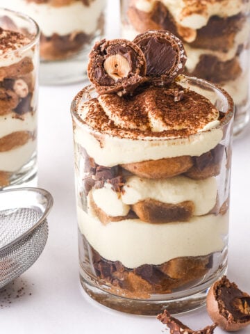 Mini tiramisu cups shown on a white counter they are decorated with Ferrero Rocher chocolates.