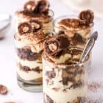 Mini Tiramisu Cups shown on a marble kitchen counter, the cup in the front has a spoonful missing.