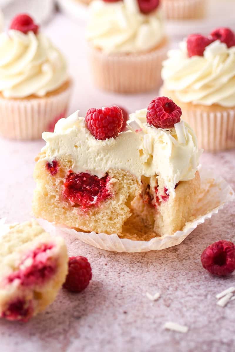 Raspberry and White Chocolate Cupcake shown sliced in half so that you can see the raspberry filling inside of the cupcake. 