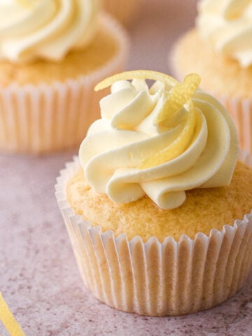 Lemon drizzle cupcake decorated with vanilla buttercream and lemon zest shown on a kitchen counter.