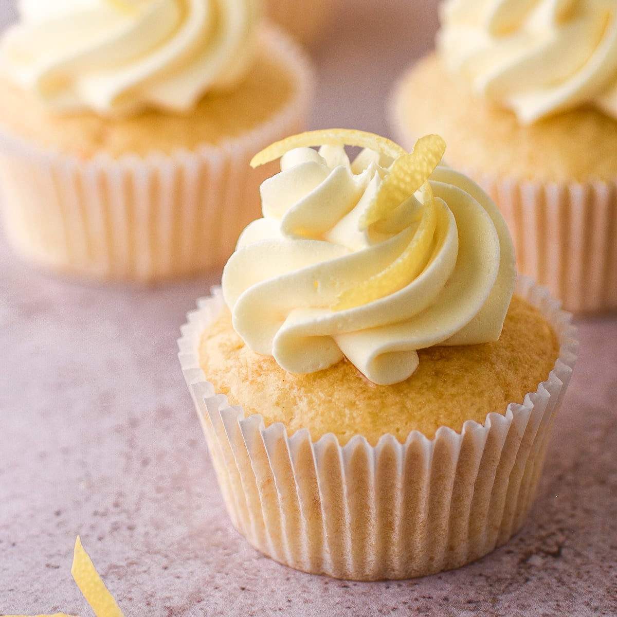 Lemon drizzle cupcake decorated with vanilla buttercream and lemon zest shown on a kitchen counter.