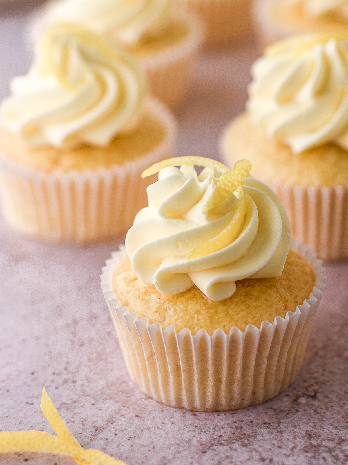 Lemon drizzle cupcake decorated with vanilla buttercream and lemon zest shown on a kitchen counter. 